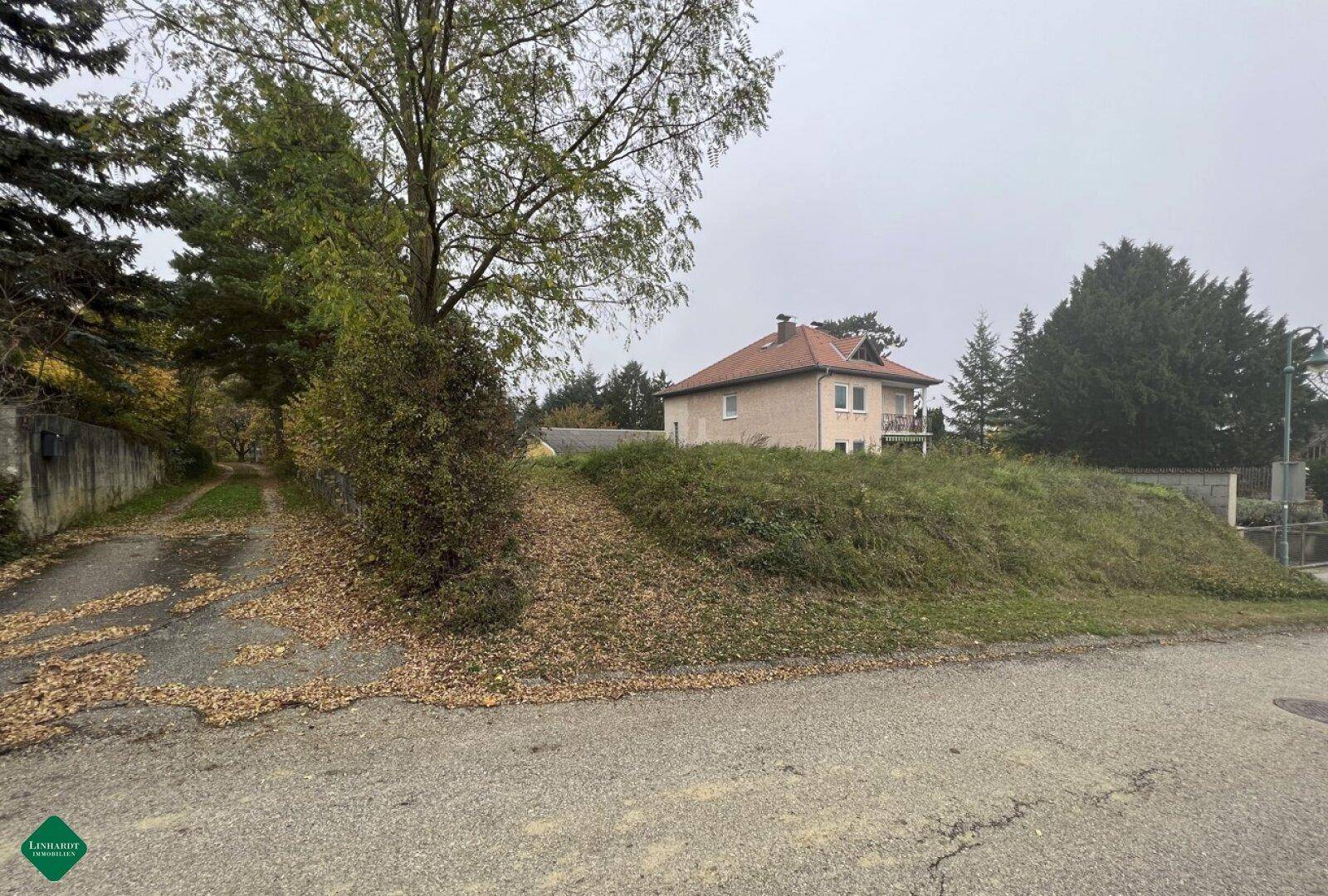 Haus auf einem Hügel mit herbstlicher Vegetation und bewölktem Himmel, umgeben von Bäumen.