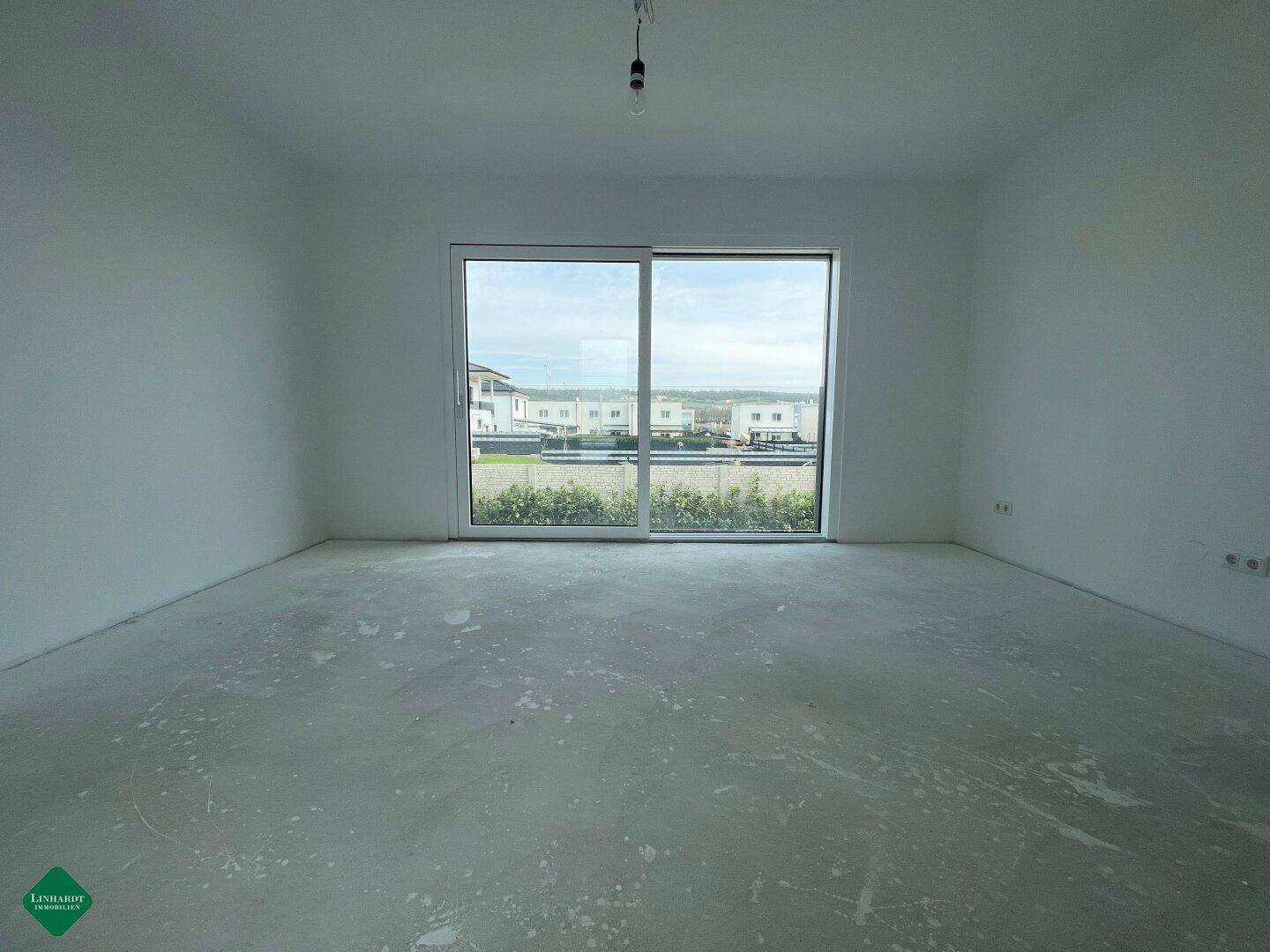 Unmöbliertes Zimmer im Rohbau mit großem Fenster und Blick auf die Nachbarschaft.