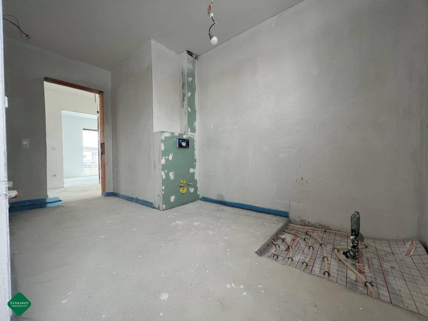 Raum im Rohbau mit sichtbaren Fußbodenheizungsrohren und unfertigen Wänden.