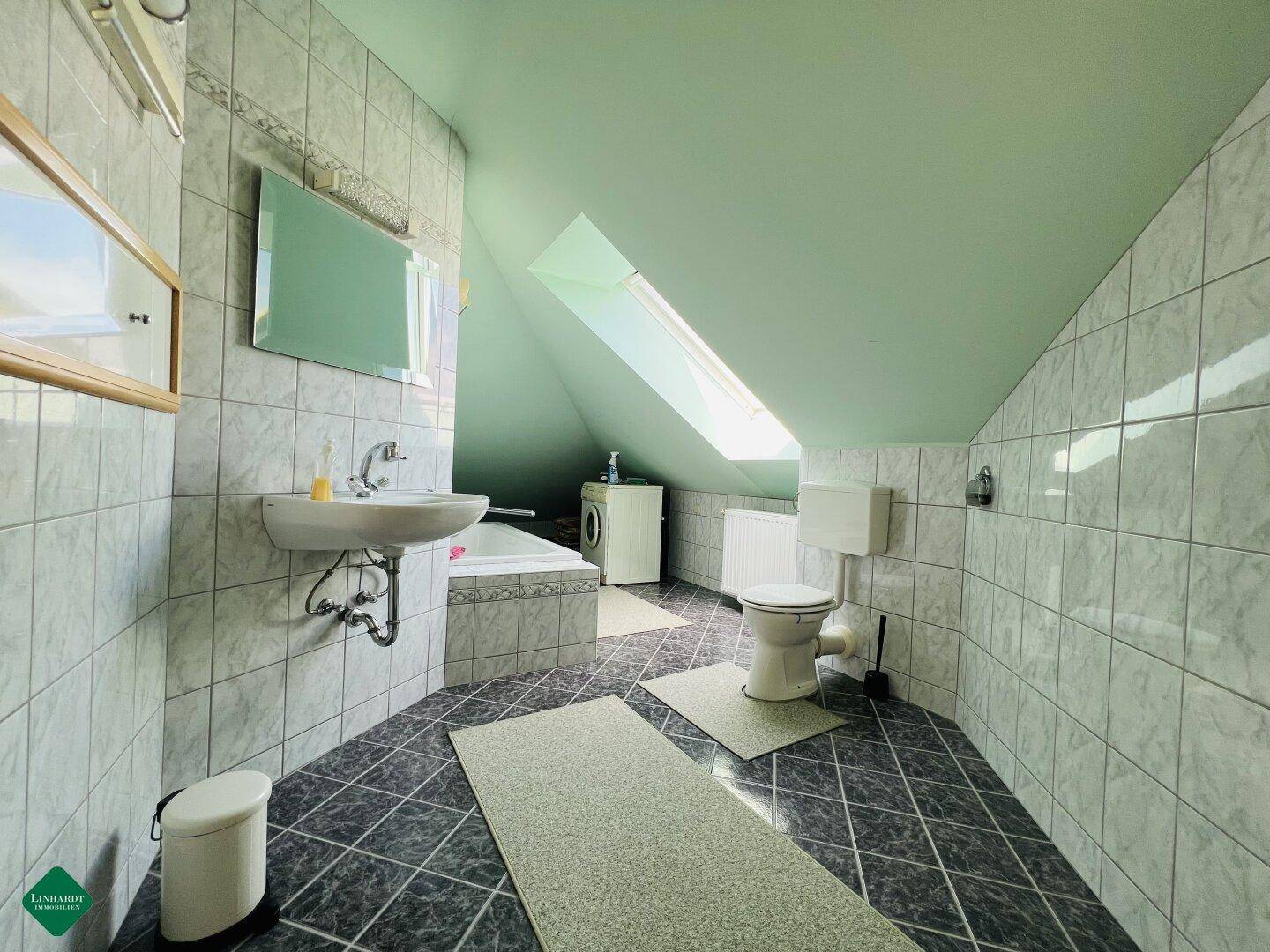 Badezimmer im Dachgeschoss mit hellgrüner Decke, Fliesen und einem Dachfenster.