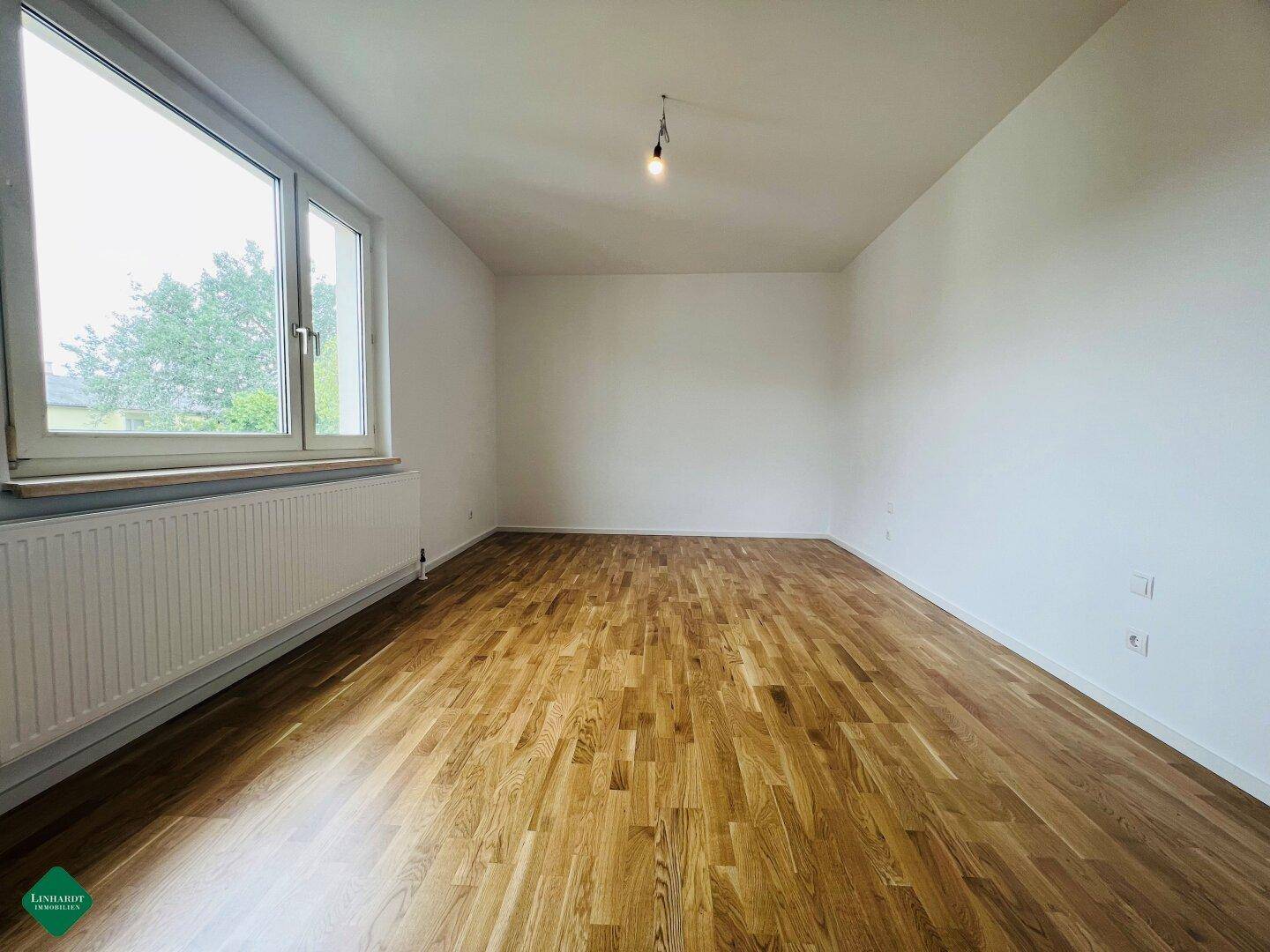 Ruhiges Zimmer mit hellem Parkettboden und großem Fenster, ideal als Schlaf- oder Arbeitszimmer.