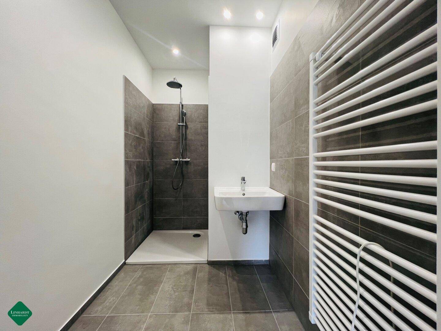 Modernes Badezimmer mit ebenerdiger Dusche, Wandwaschbecken und beheiztem Handtuchhalter.