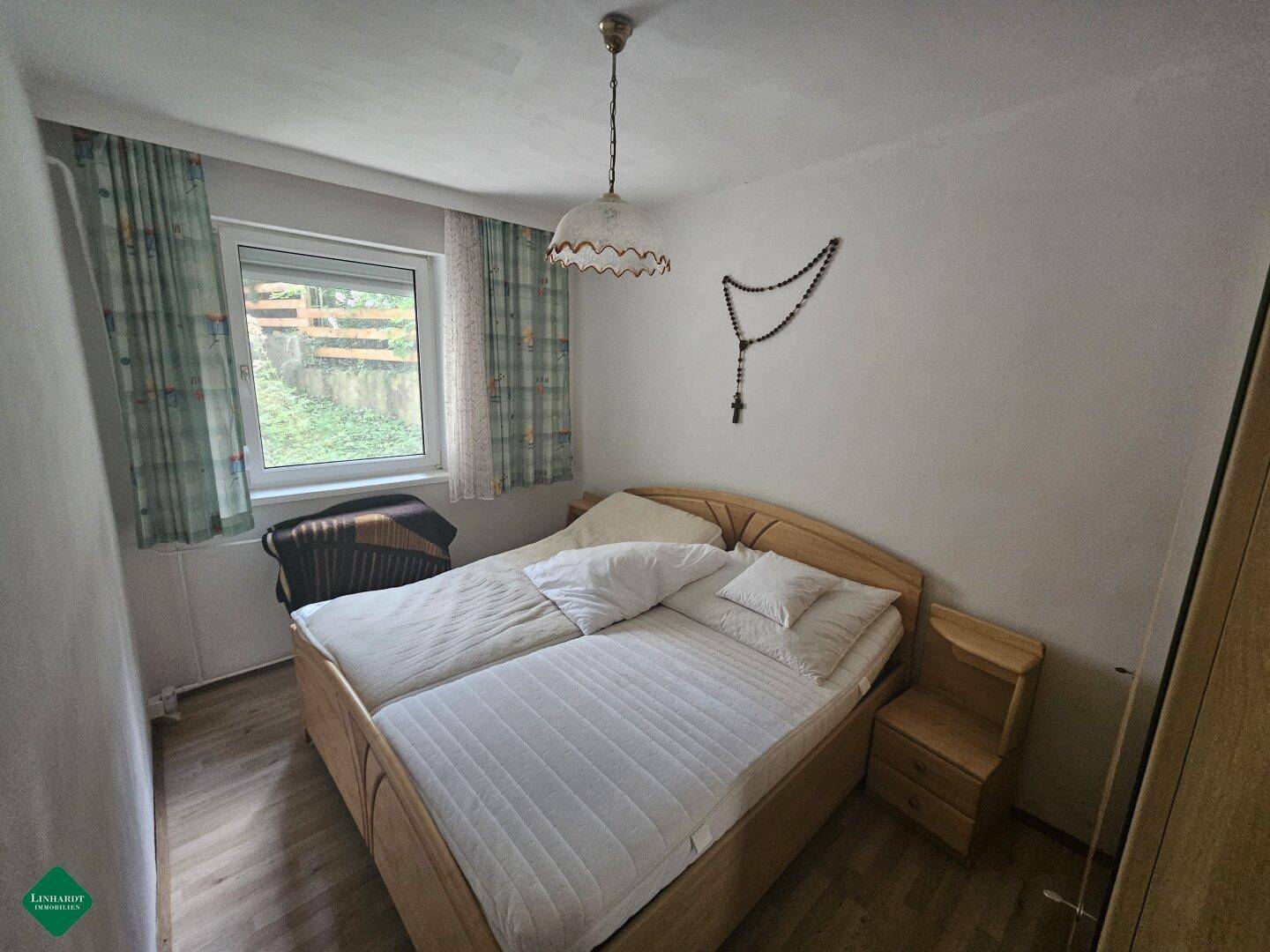 Helles Schlafzimmer mit Doppelbett, Holzmöbeln und Fenster mit Blick ins Grüne.