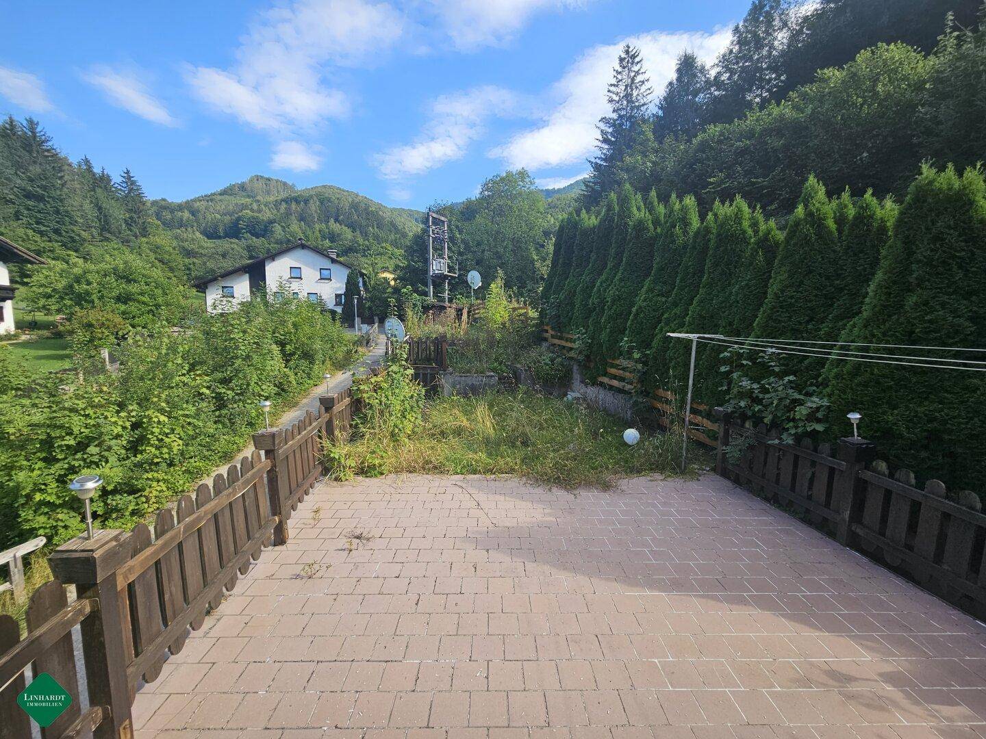 Große gepflasterte Terrasse mit Holzzaun und weitem Blick auf die umliegende Landschaft.