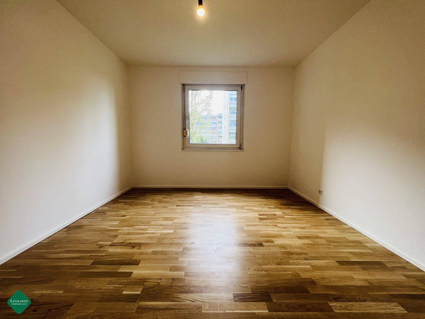 Ruhiges Schlafzimmer mit Holzboden und einem Fenster mit Blick ins Grüne.