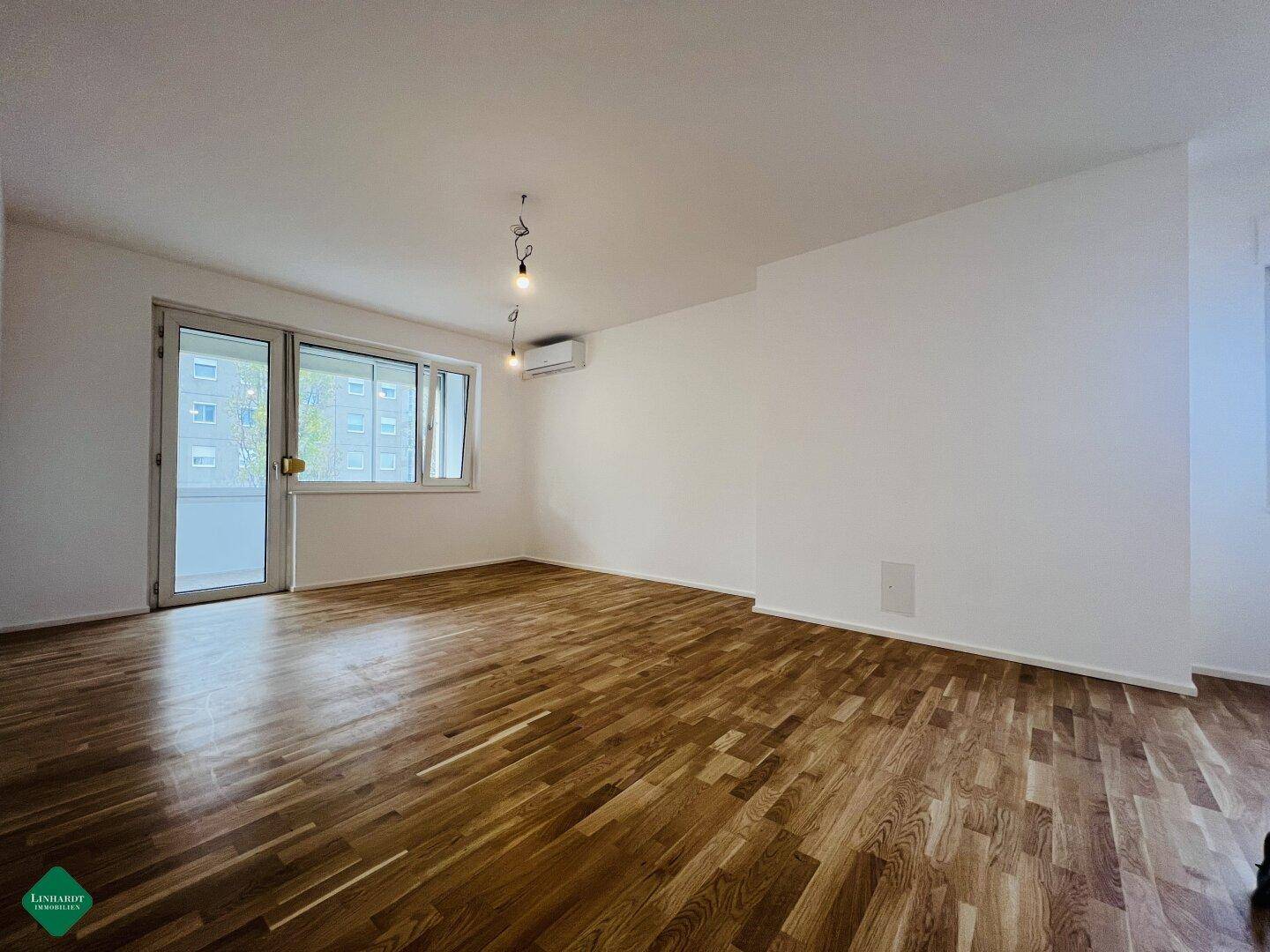 Helles, frisch renoviertes Wohnzimmer mit neuem Parkettboden und Zugang zum Balkon.