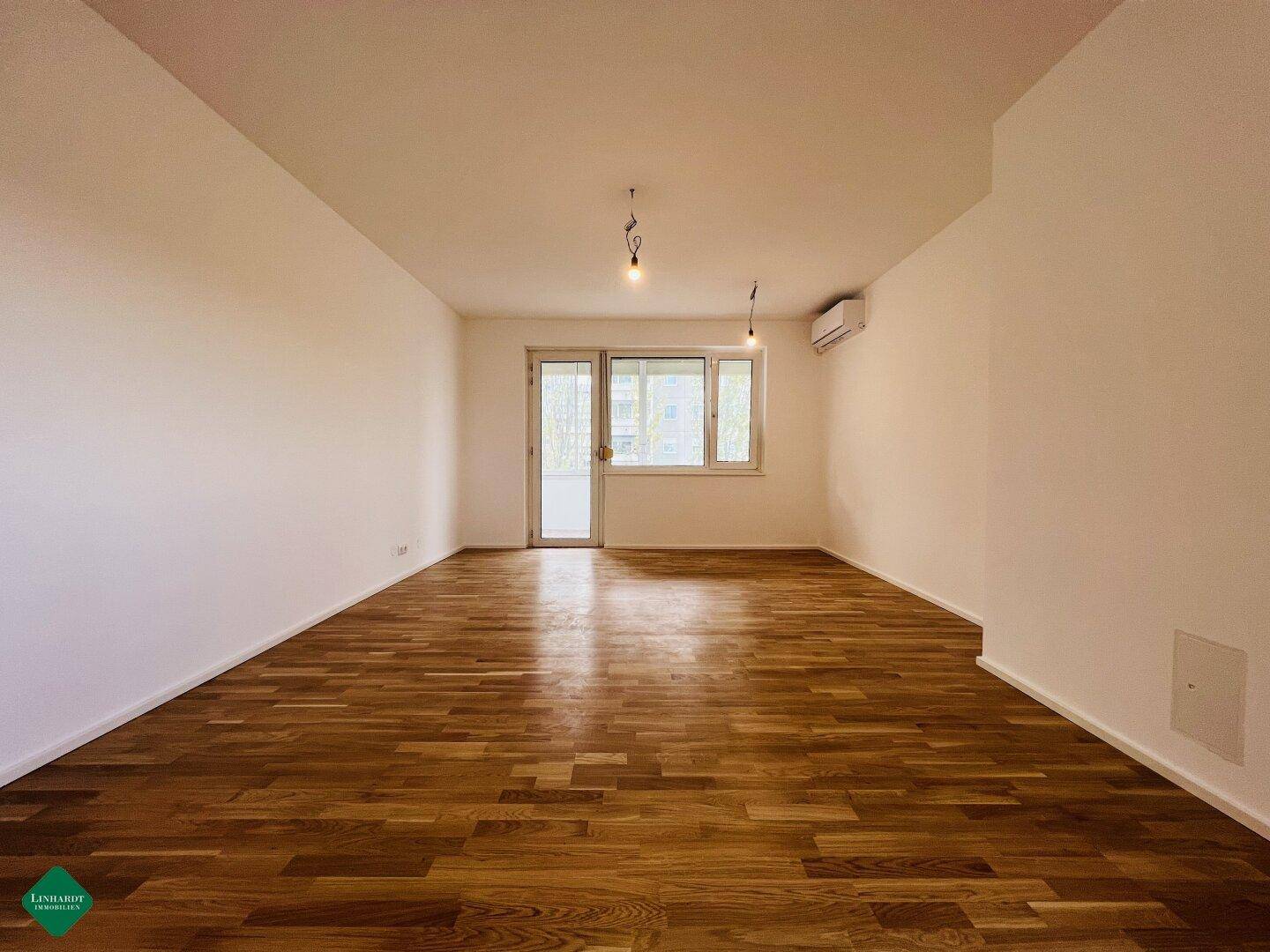 Geräumiges Wohnzimmer mit glänzendem Parkettboden und viel Tageslicht, ideal für individuelle Gestaltung.