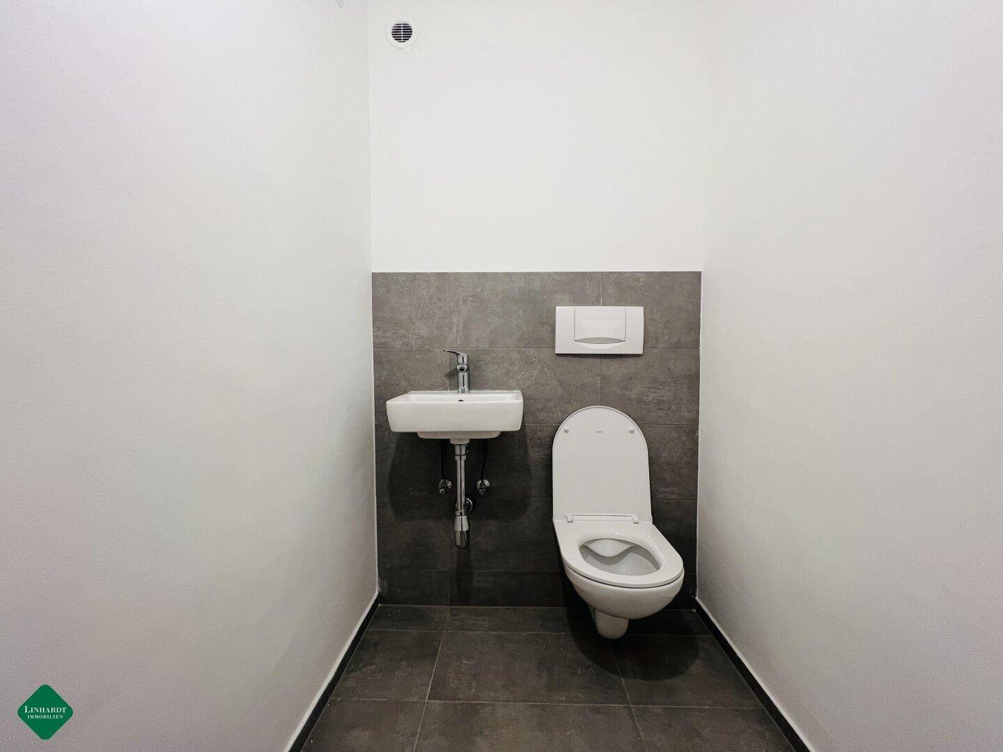 Separates Gäste-WC mit modernem Wand-WC, kleinem Waschbecken und Abluftventilator.