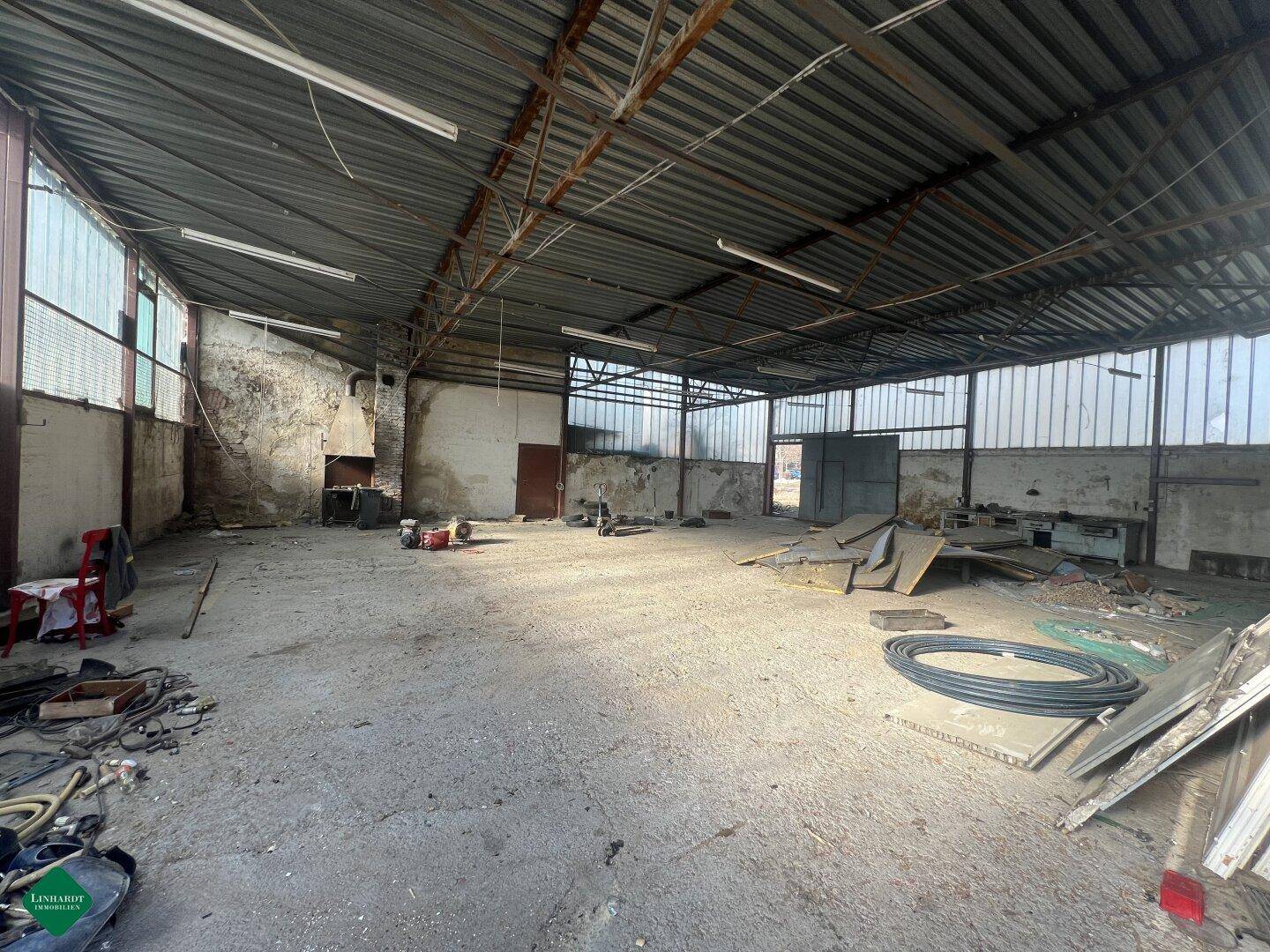 Große, leere Lagerhalle mit Betonboden, hohen Decken und viel natürlichem Licht durch Fenster.