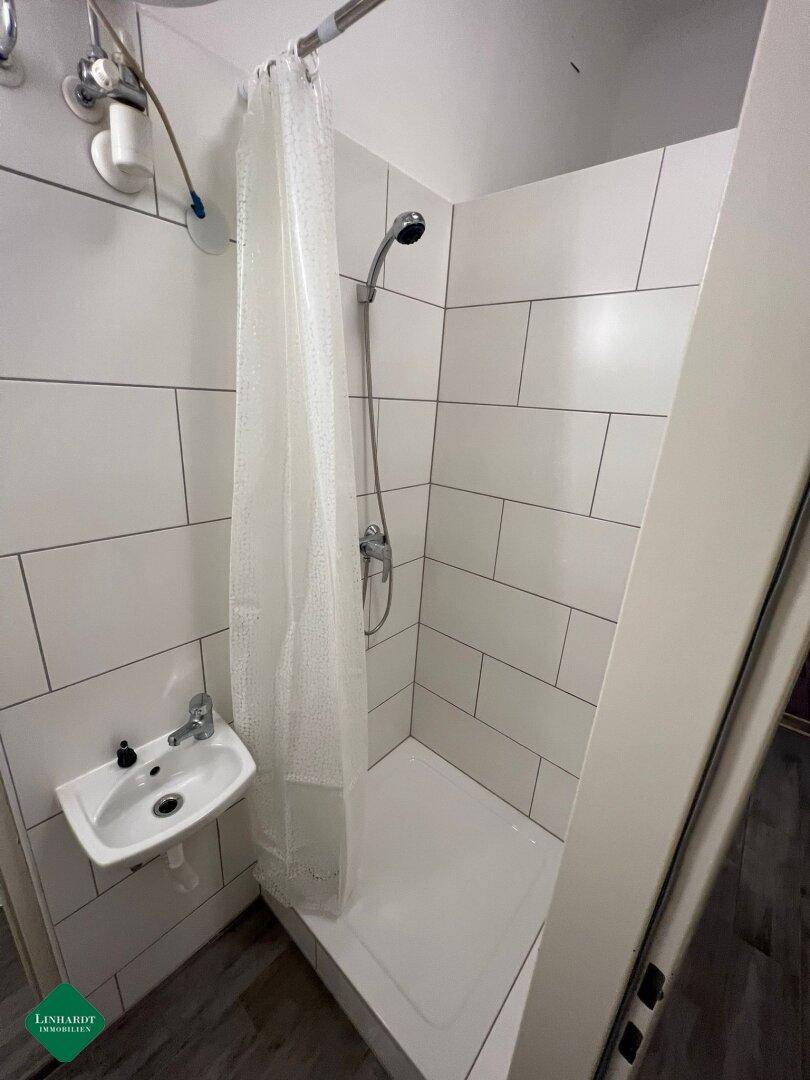 Funktionale Dusche mit weißen Fliesen, Duschvorhang und kleinem Waschbecken.