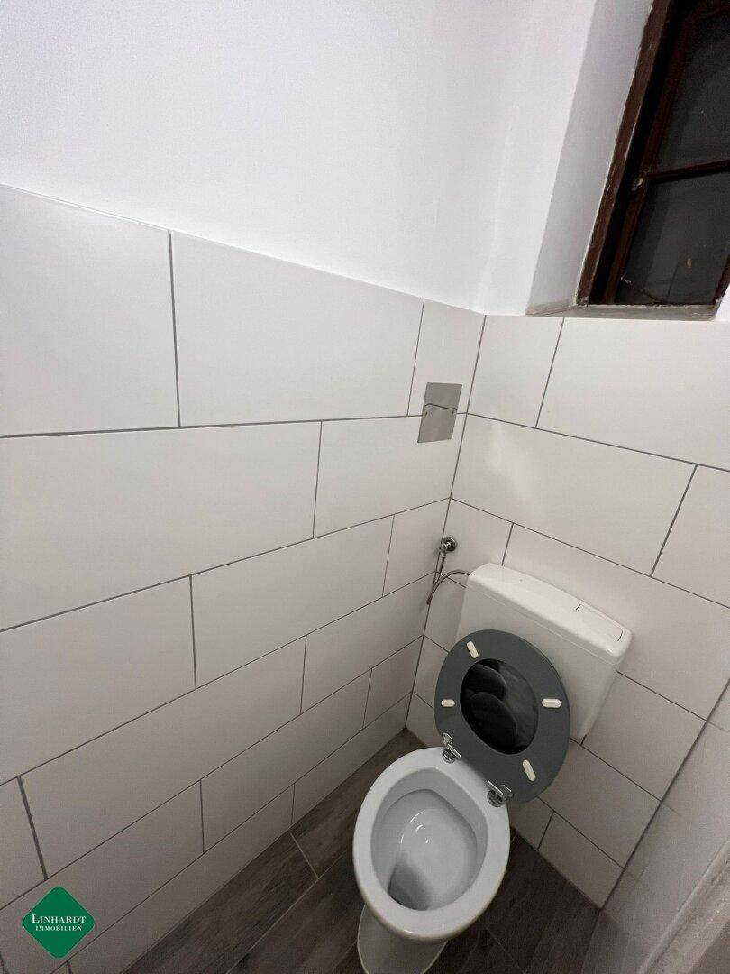 Separates WC mit weißen Wandfliesen und einem kleinen Fenster für Belüftung.
