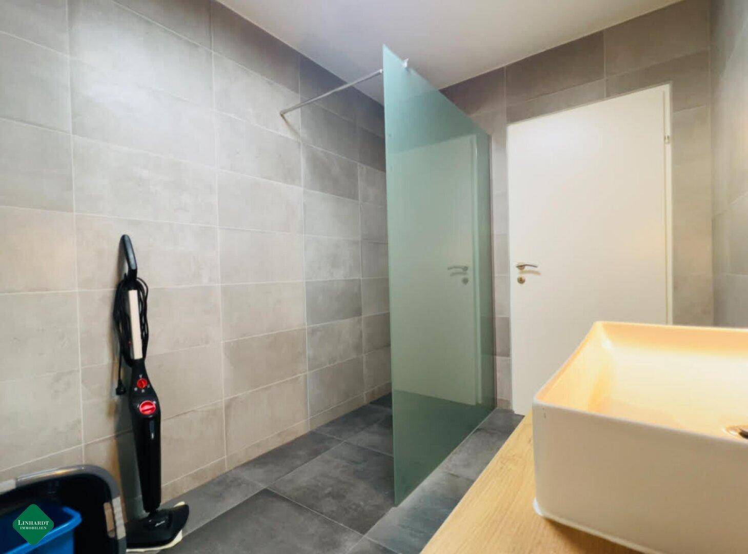 Modernes Badezimmer mit begehbarer Dusche und grauen Fliesen.