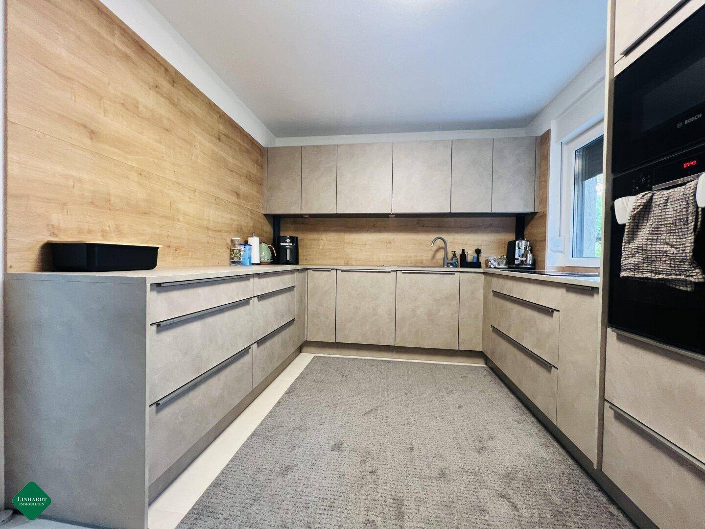 Moderne Küche mit hellgrauen Fronten, Holzwandverkleidung und integrierten Geräten.