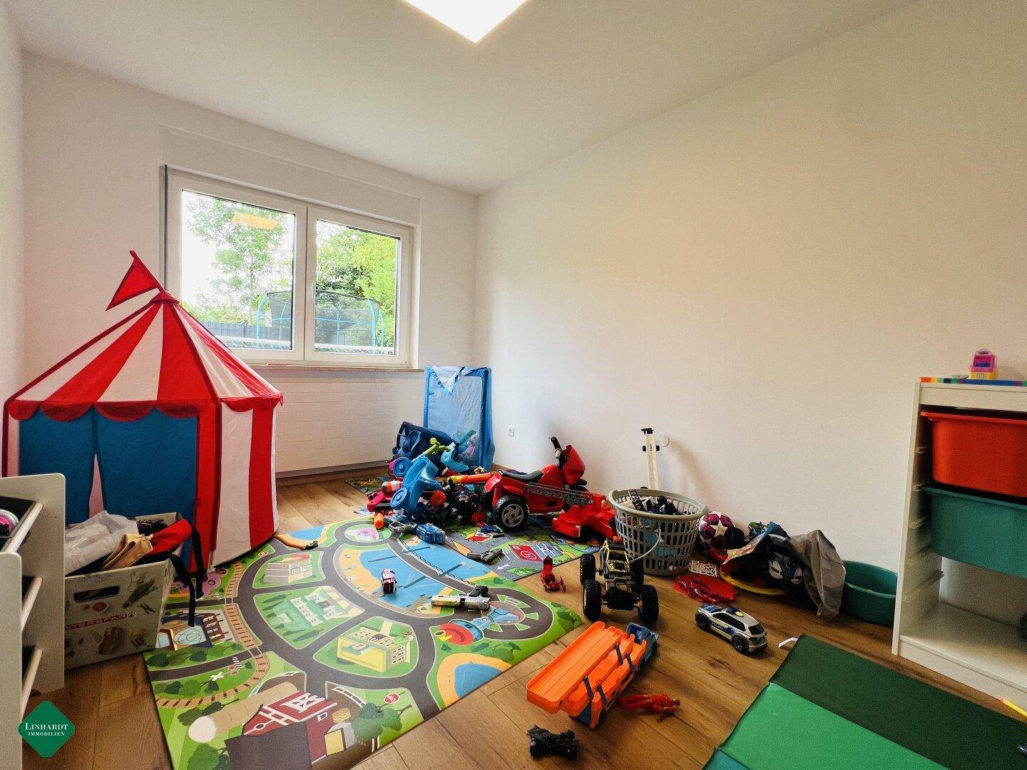 Helles Kinderzimmer mit Holzboden, großem Fenster und Spielbereich.