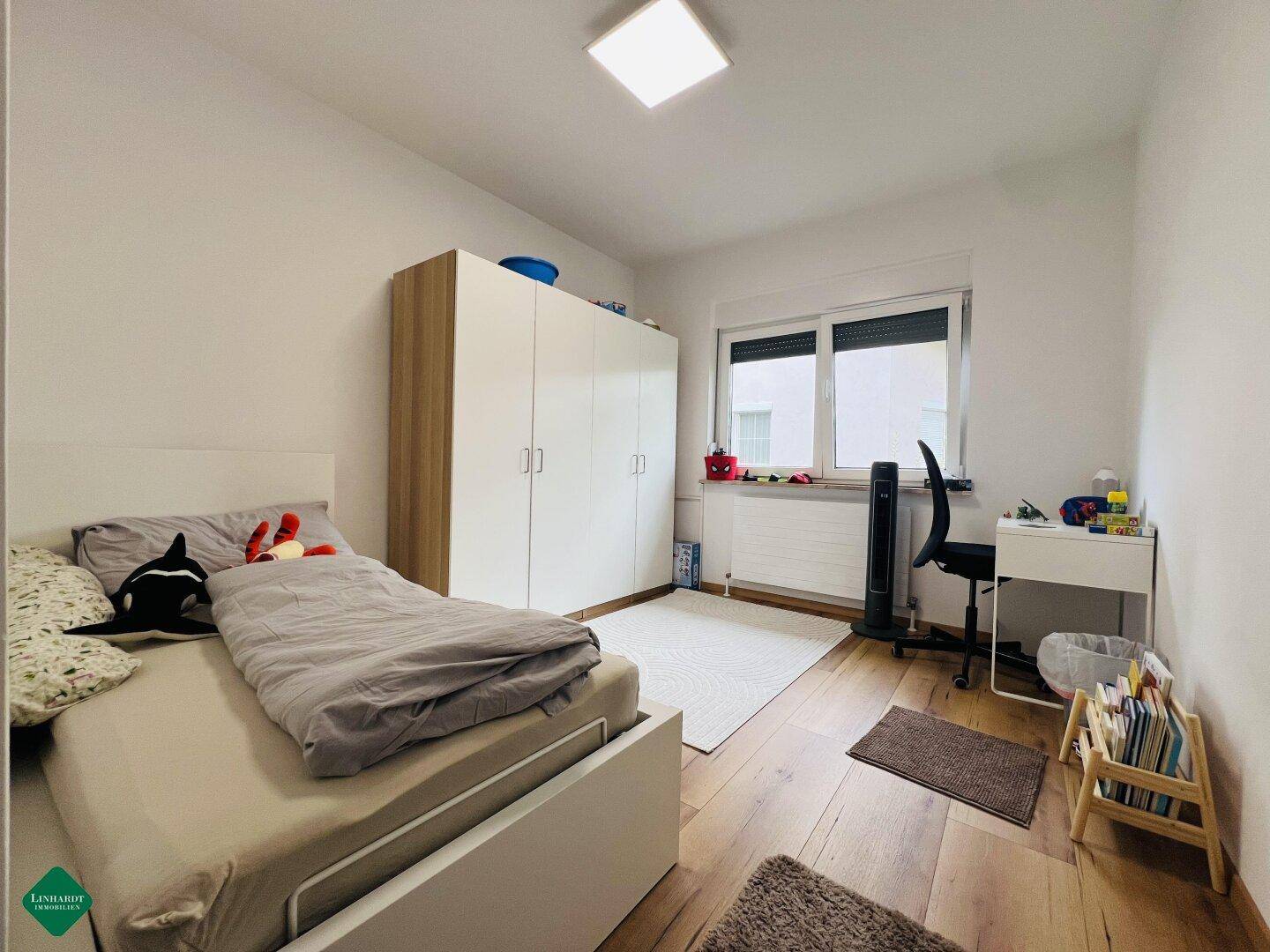 Kinderzimmer mit Holzboden, großem Fenster und einem Kleiderschrank.