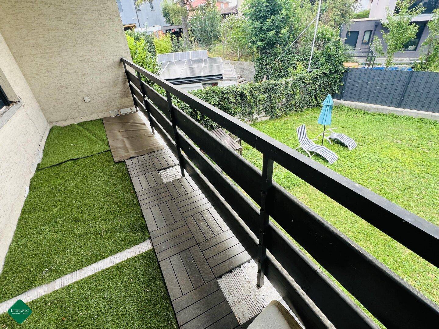 Balkon mit Kunstrasen und Holzdielen, bietet Blick auf den Garten.