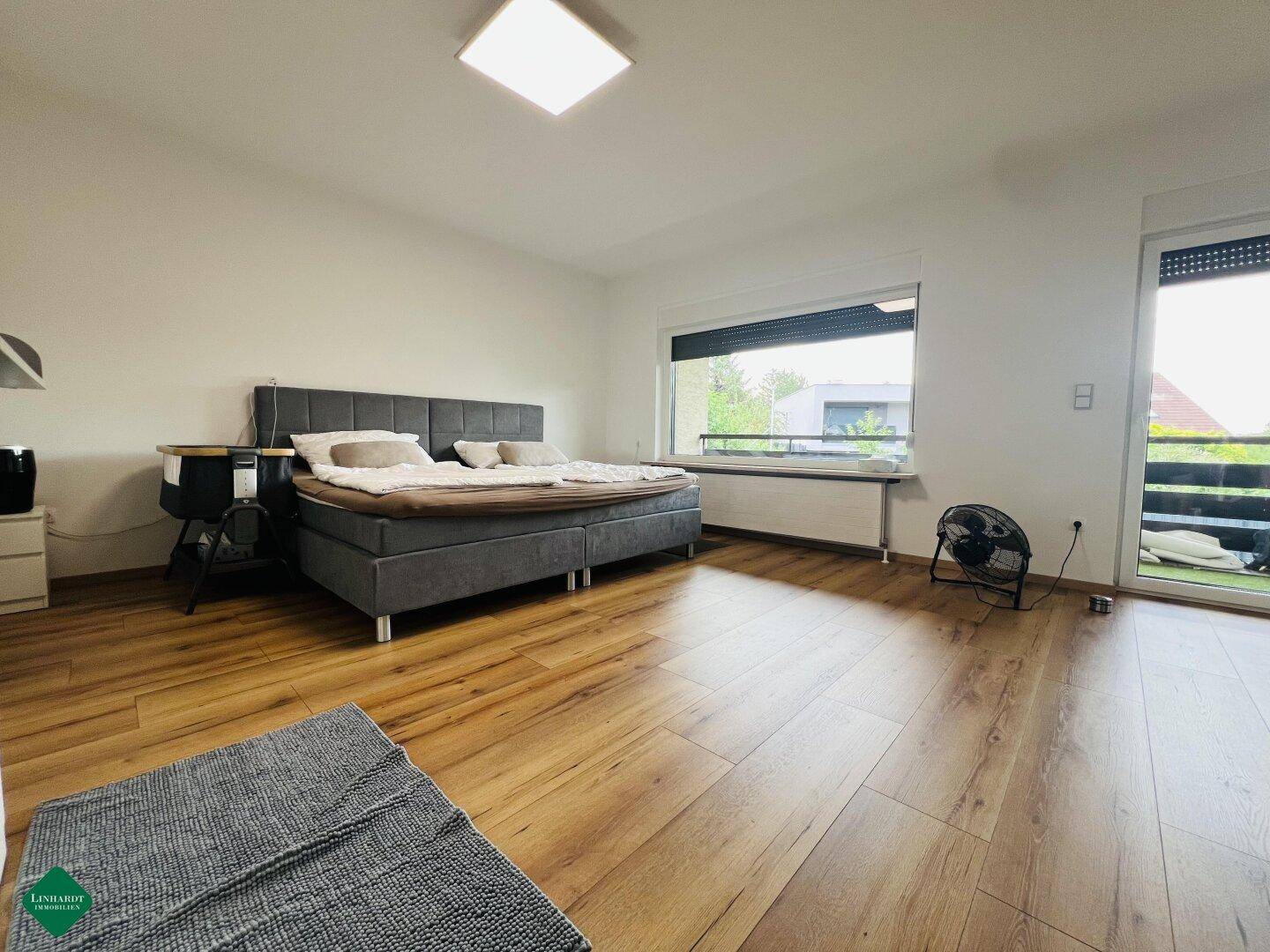 Helles Schlafzimmer mit Holzboden, großem Fenster und Zugang zum Balkon.