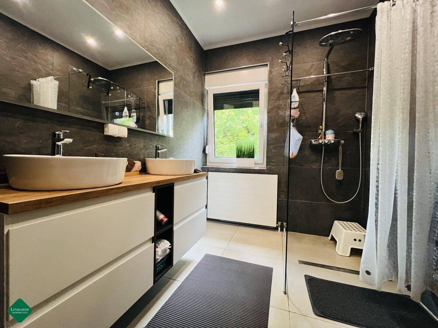 Elegantes Badezimmer mit Doppelwaschbecken, großer Dusche und Fenster.