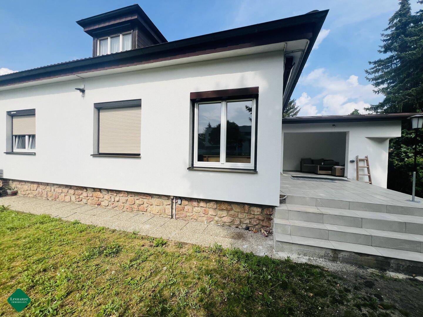 Seitenansicht des Hauses mit einer gepflasterten Terrasse und einem überdachten Bereich.