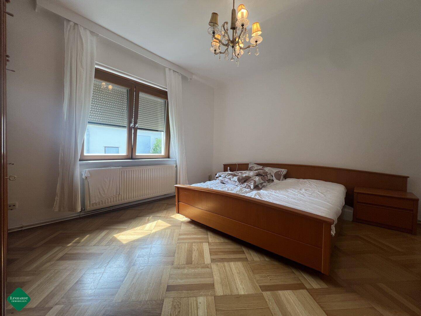 Helles Schlafzimmer mit Doppelbett, Parkettboden und Fenster mit Rollladen.