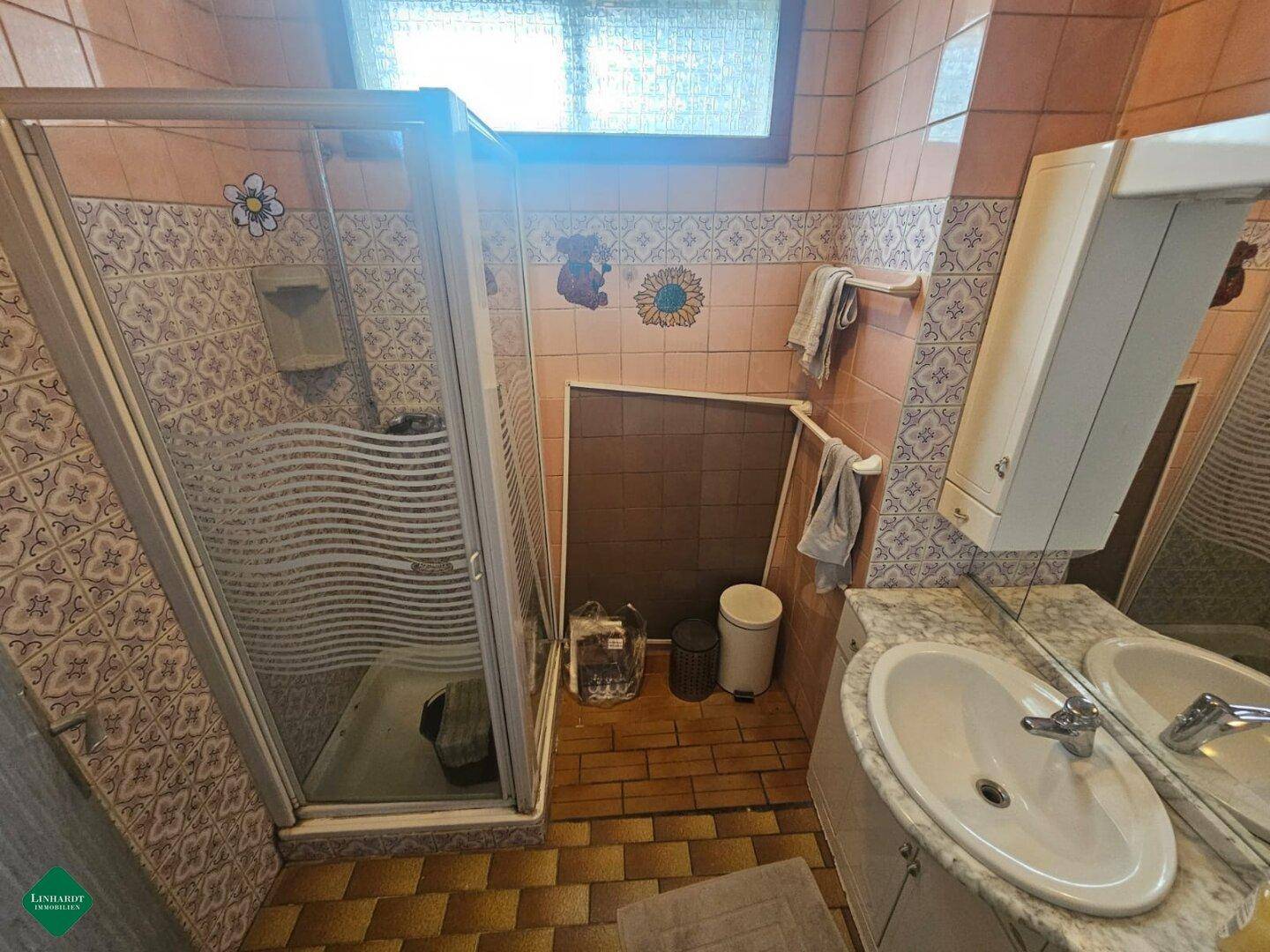 Badezimmer mit Duschkabine, Waschbecken und Fliesen im charakteristischen 80er-Jahre-Stil.