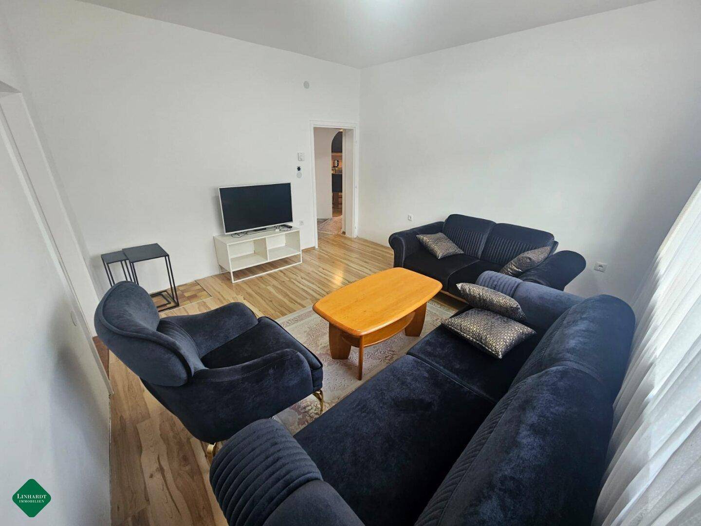 Helles Wohnzimmer mit bequemen Sofas, Teppich und Blick auf den angrenzenden Flur.