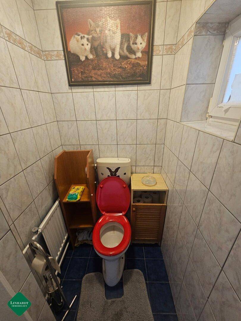 Separate Toilette mit Fliesen, Fenster und einem auffälligen roten Toilettensitz.
