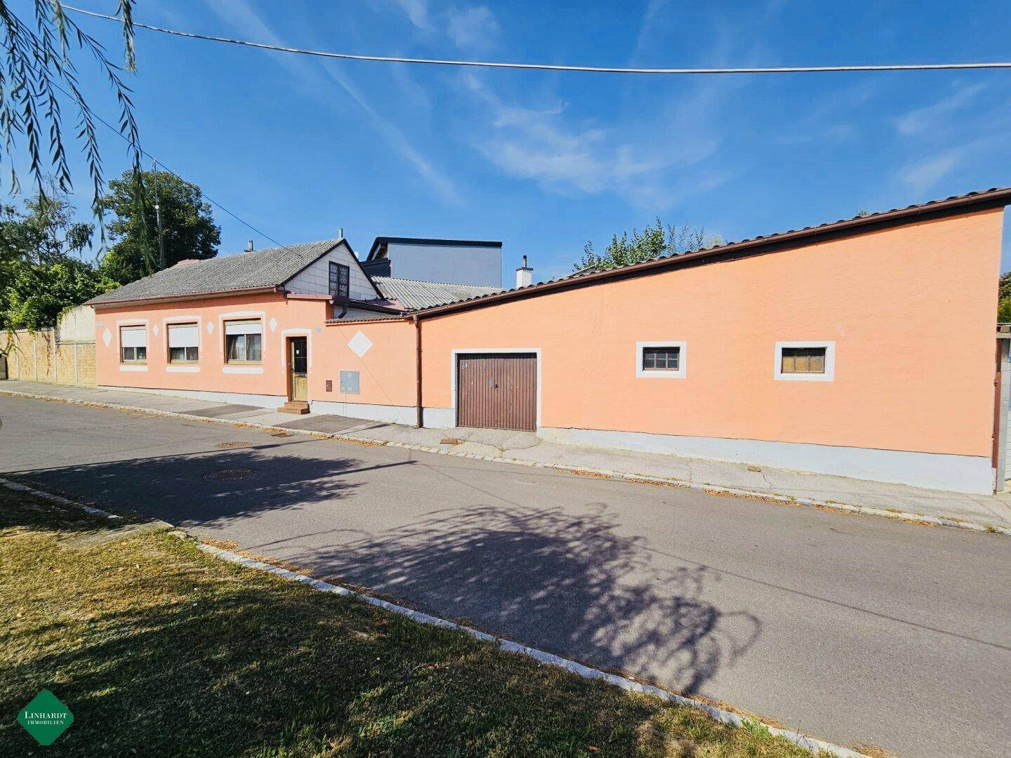 Seitenansicht des Wohnhauses mit orangefarbener Fassade, Garagentor und klarem blauem Himmel.