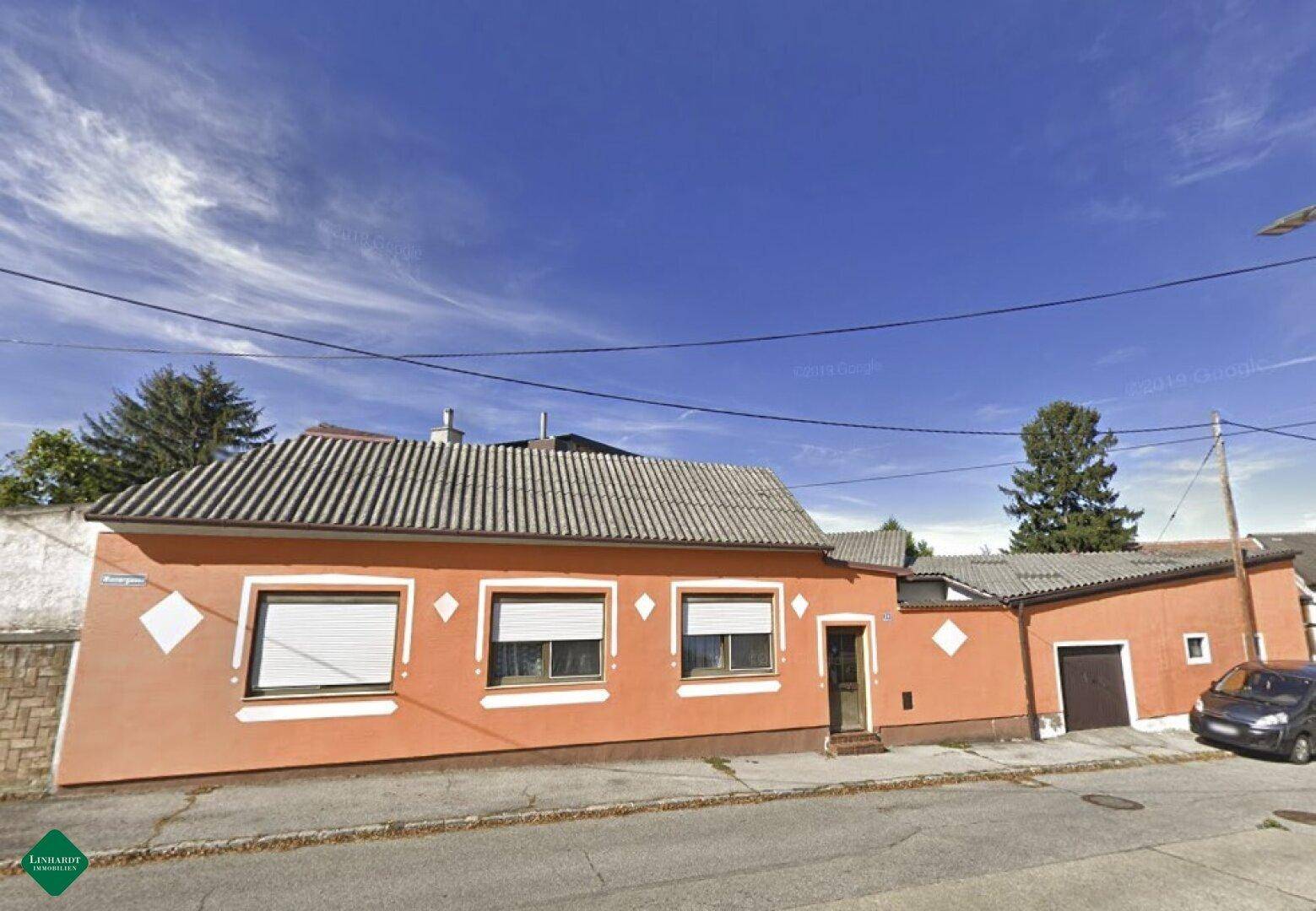 Vorderansicht des Hauses mit orangefarbener Fassade, Rollläden an den Fenstern und Satteldach.