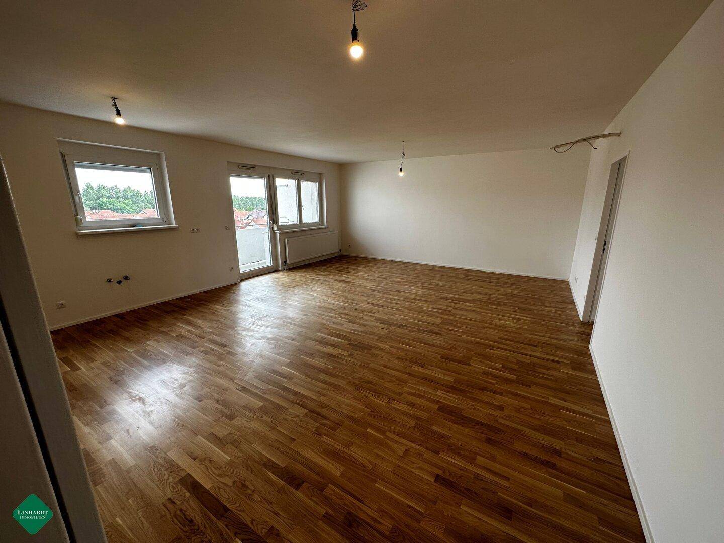 Helles, leeres Wohnzimmer mit schönem Parkettboden und Zugang zu einem Balkon, bereit zur individuellen Gestaltung.