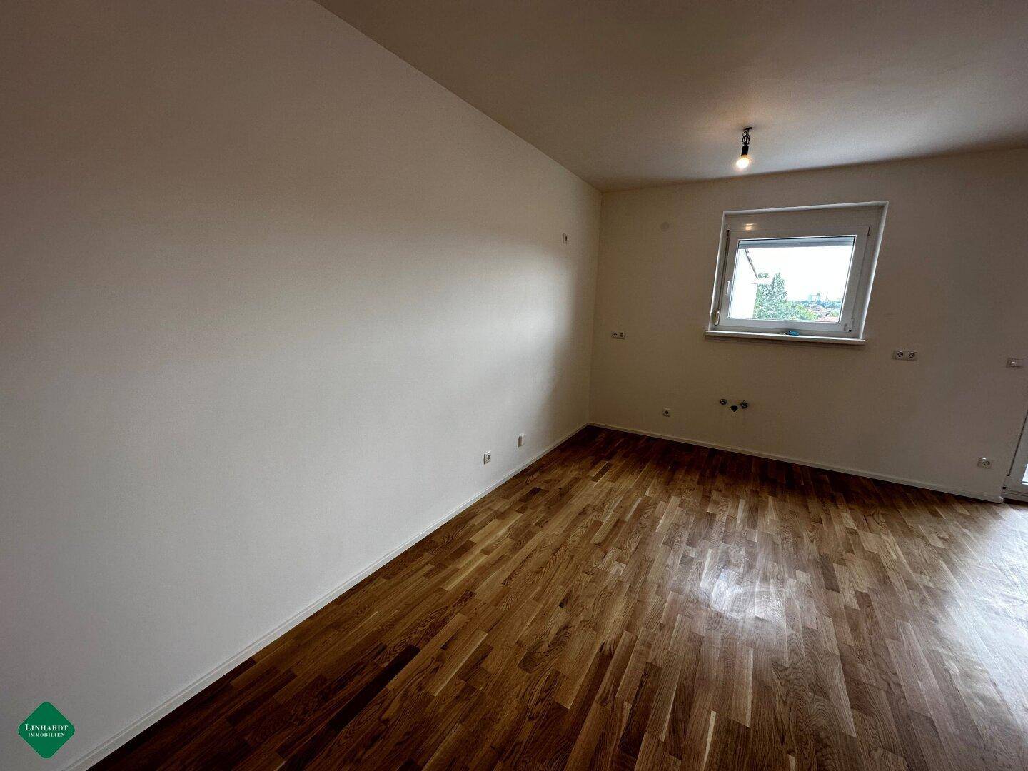 Geräumiges, unmöbliertes Zimmer mit glänzendem Parkettboden und einem großen Fenster für natürliche Belichtung.