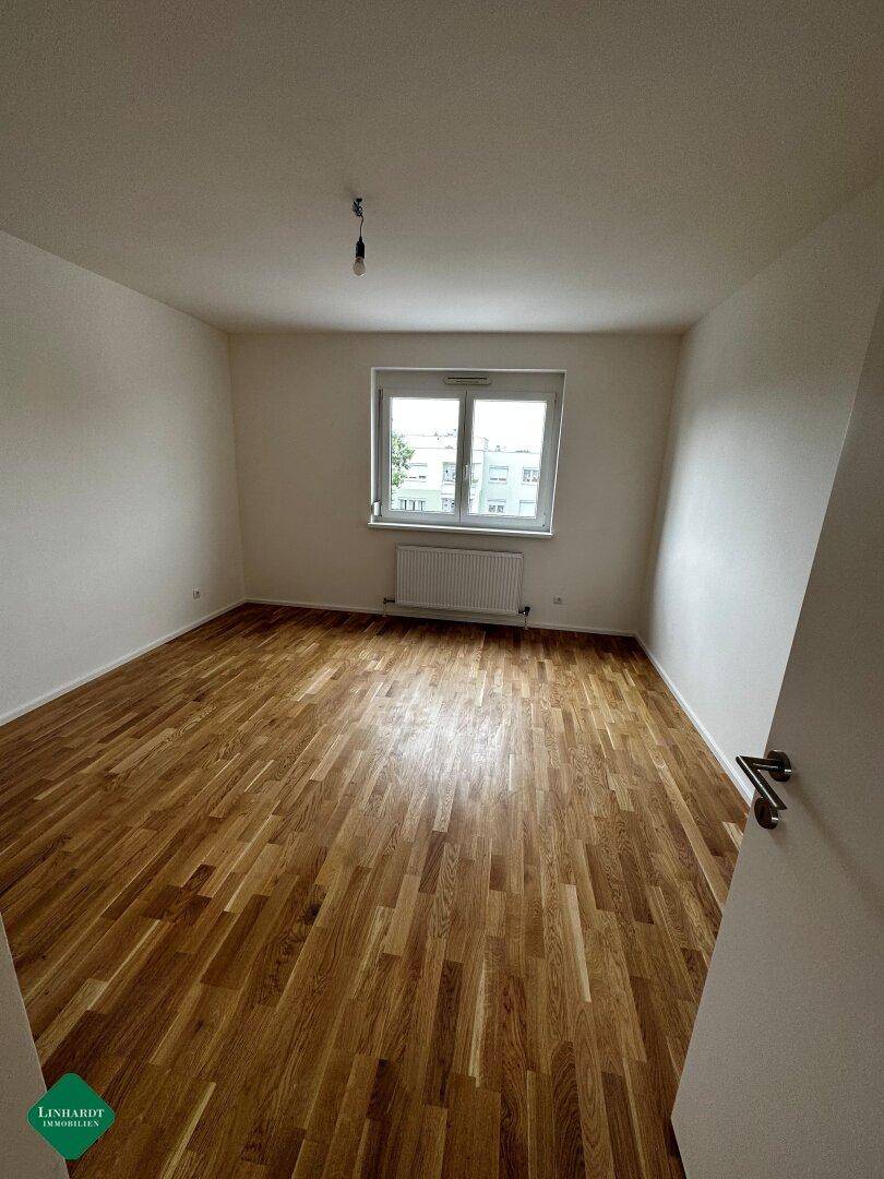 Unmöbliertes Zimmer mit ansprechendem Parkettboden und einem Fenster, das für eine angenehme Helligkeit sorgt.