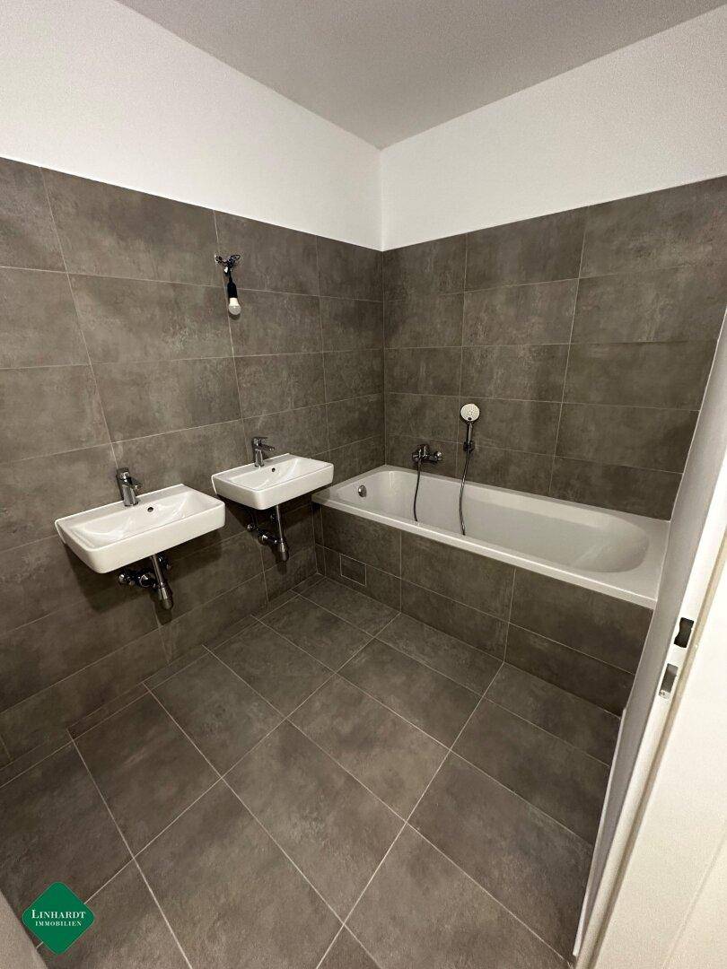 Modernes Badezimmer mit grauen Fliesen, einer Badewanne und zwei Waschbecken für Komfort und Funktionalität.