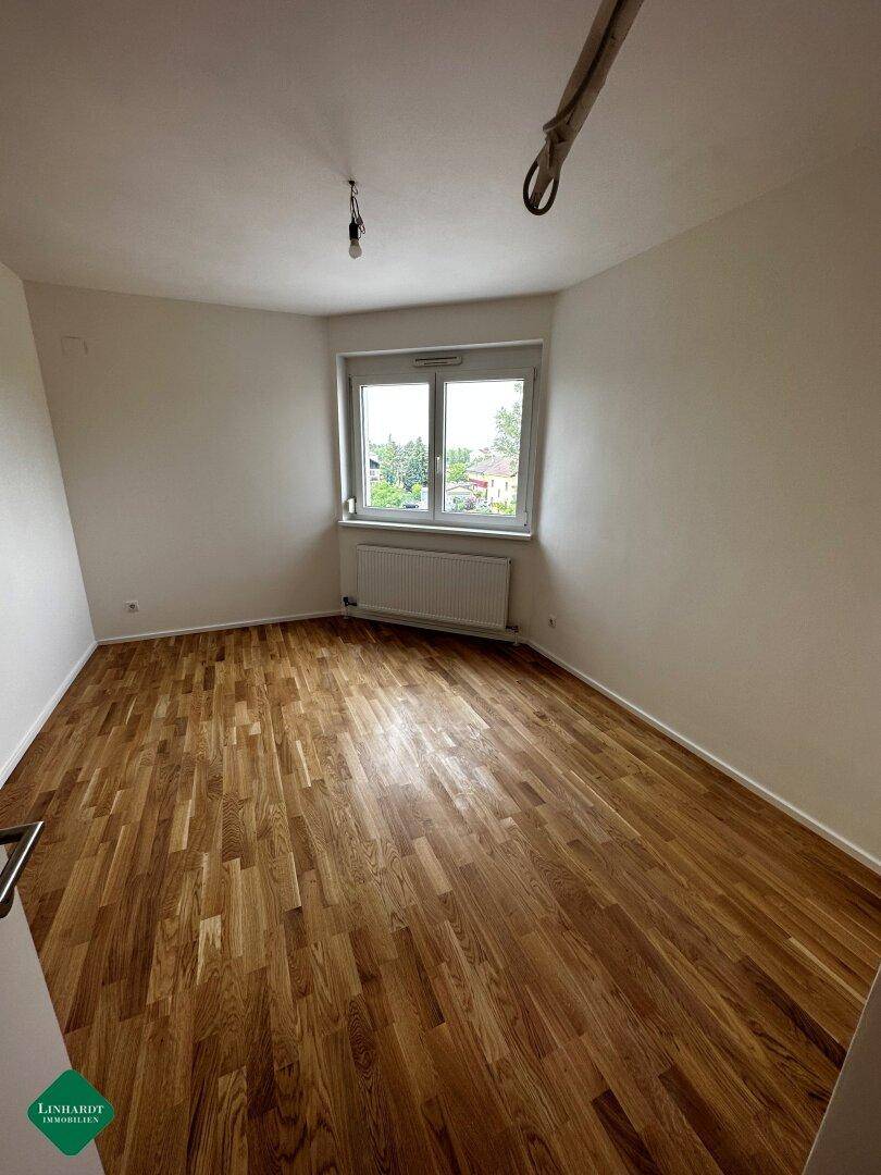 Helles Schlafzimmer mit klassischem Parkettboden und einem Fenster, das einen Blick ins Grüne bietet.