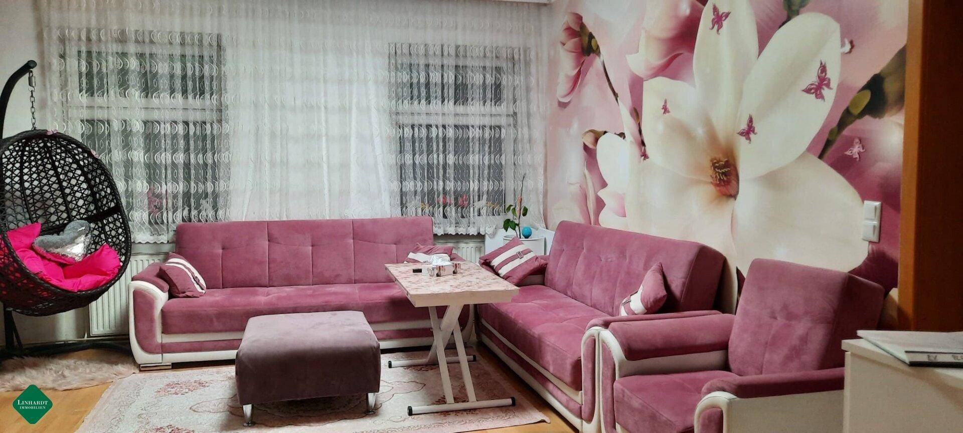 Gemütliches Wohnzimmer mit rosa Sofas, floraler Tapete und einem Hängesessel.