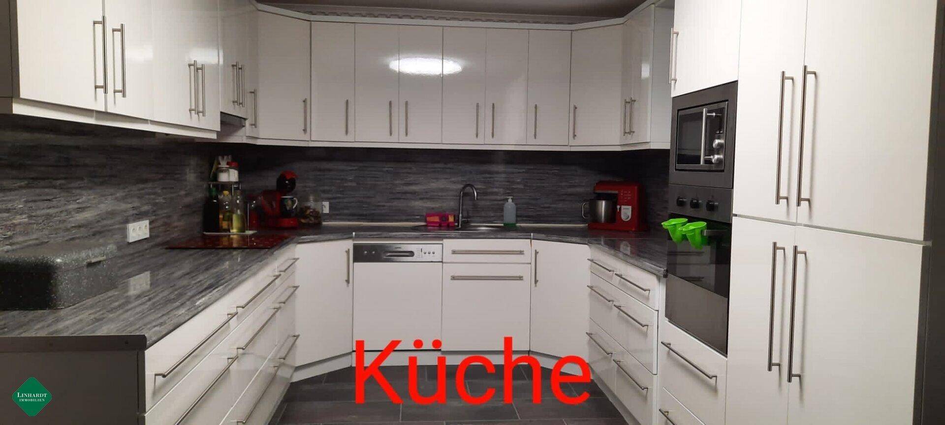 Helle Einbauküche in Weiß mit modernen Geräten und dunklen Arbeitsflächen.