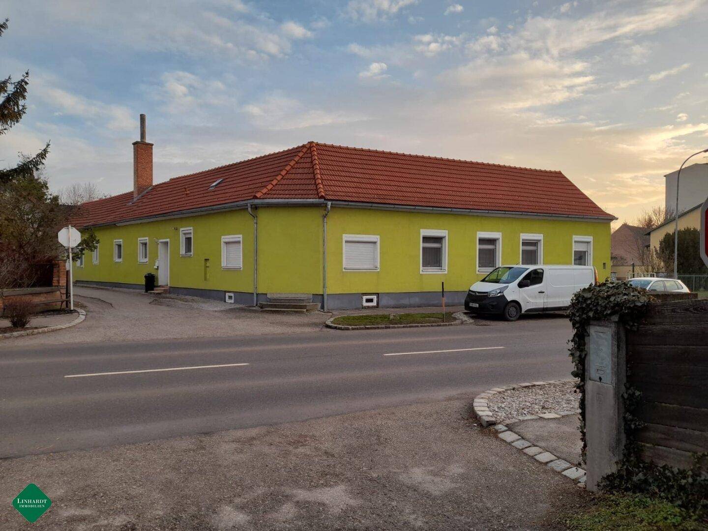 Gelb gestrichenes Gebäude mit rotem Ziegeldach an einer ruhigen Straße gelegen.