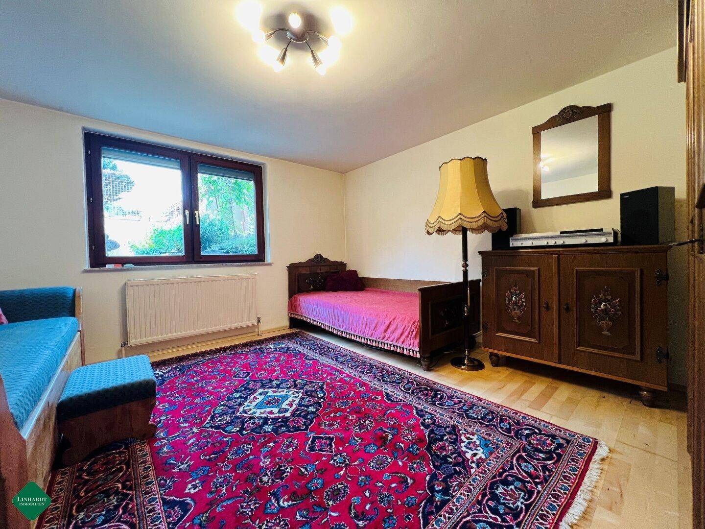 Schlafzimmer mit Einzelbett, traditionellen Holzmöbeln und einem großen, gemusterten Teppich.