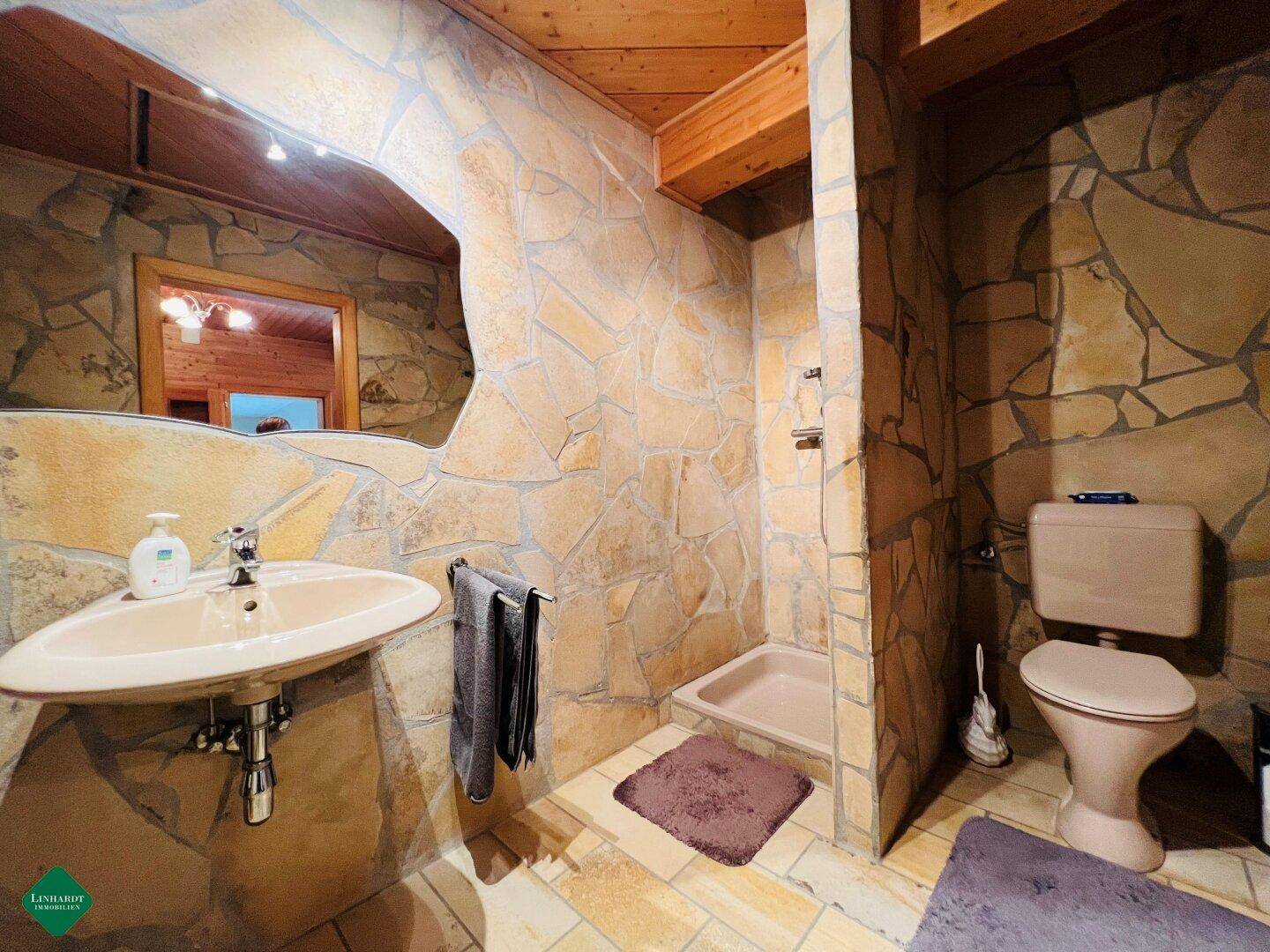 Rustikales Badezimmer mit Steinwandverkleidung, Waschbecken und Duschbereich.