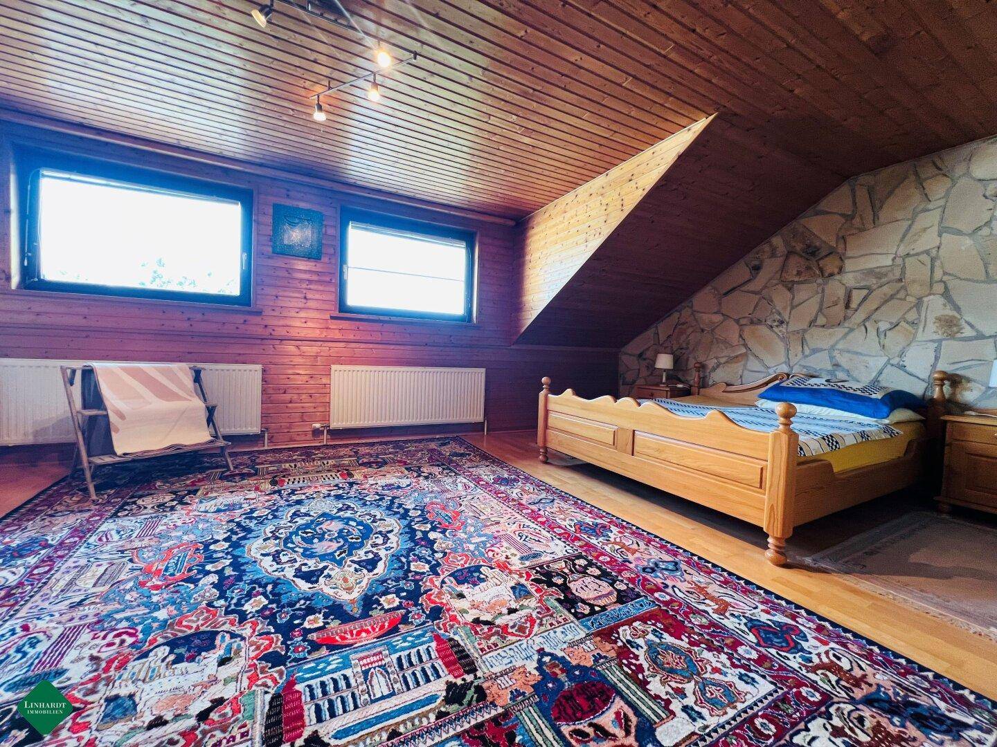Geräumiges Schlafzimmer mit Holzverkleidung, großem Teppich und Dachschräge.