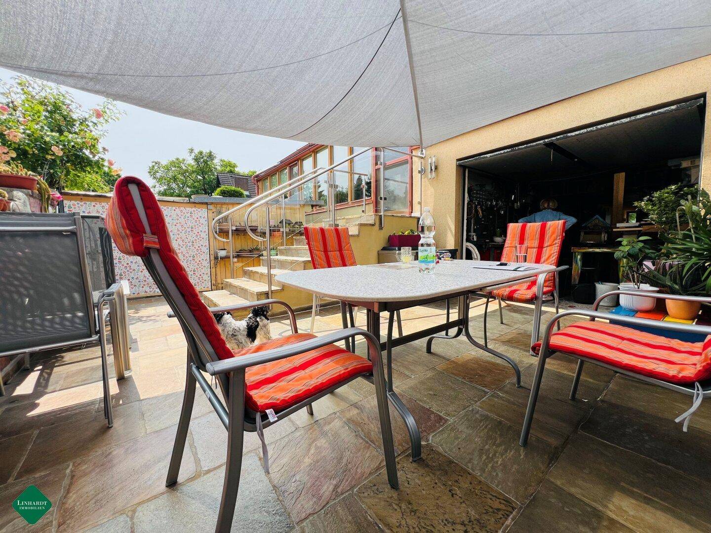 Geräumige Terrasse mit Essbereich im Freien und Zugang zu einem Garagen- oder Abstellbereich.