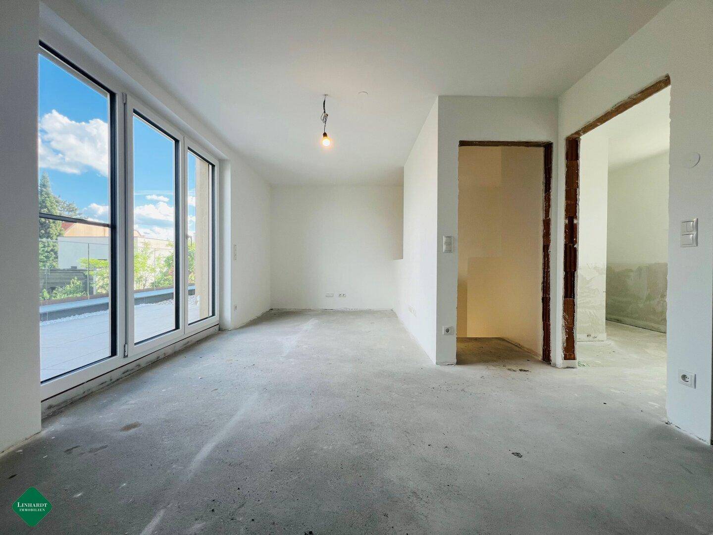 Geräumiger Wohnbereich im Rohbau mit großen Fenstern und direktem Zugang zur Terrasse.
