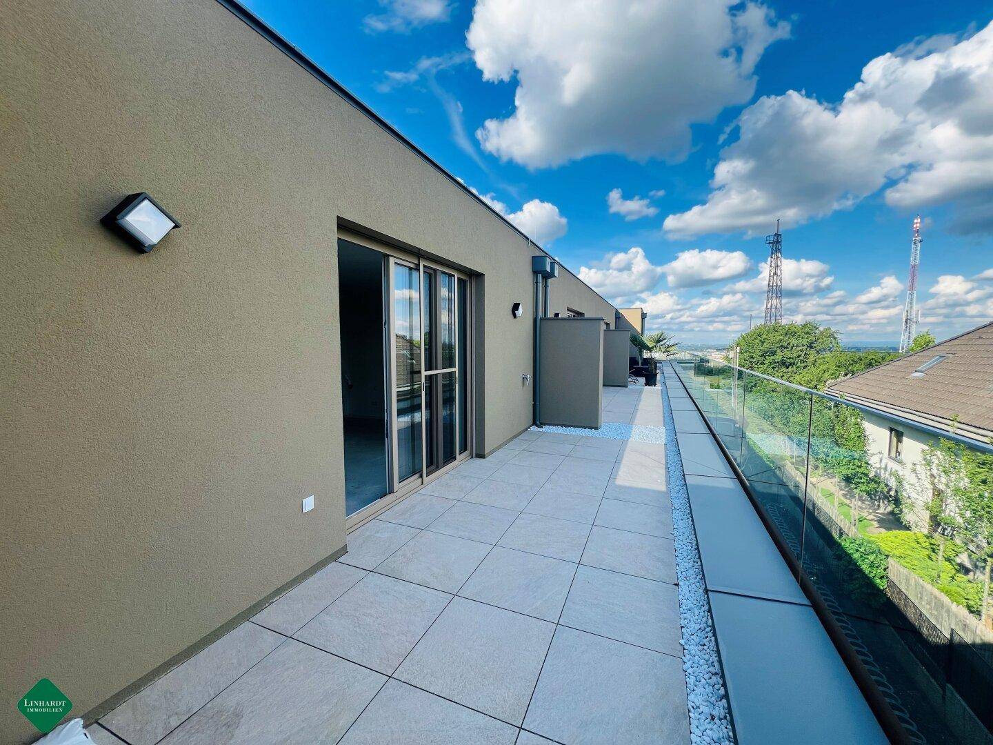 Großzügige Dachterrasse mit modernen Fliesen, Glasgeländer und weitem Blick über die Umgebung.