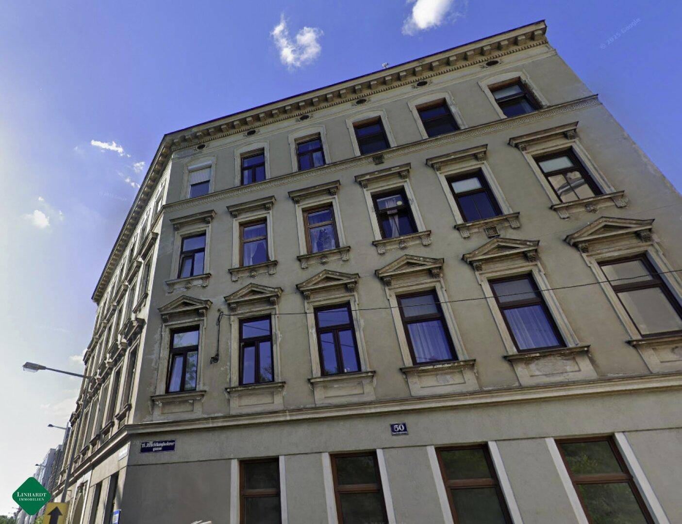 Historisches Mehrfamilienhaus mit klassischer Architektur und gut erhaltener Fassade unter blauem Himmel.