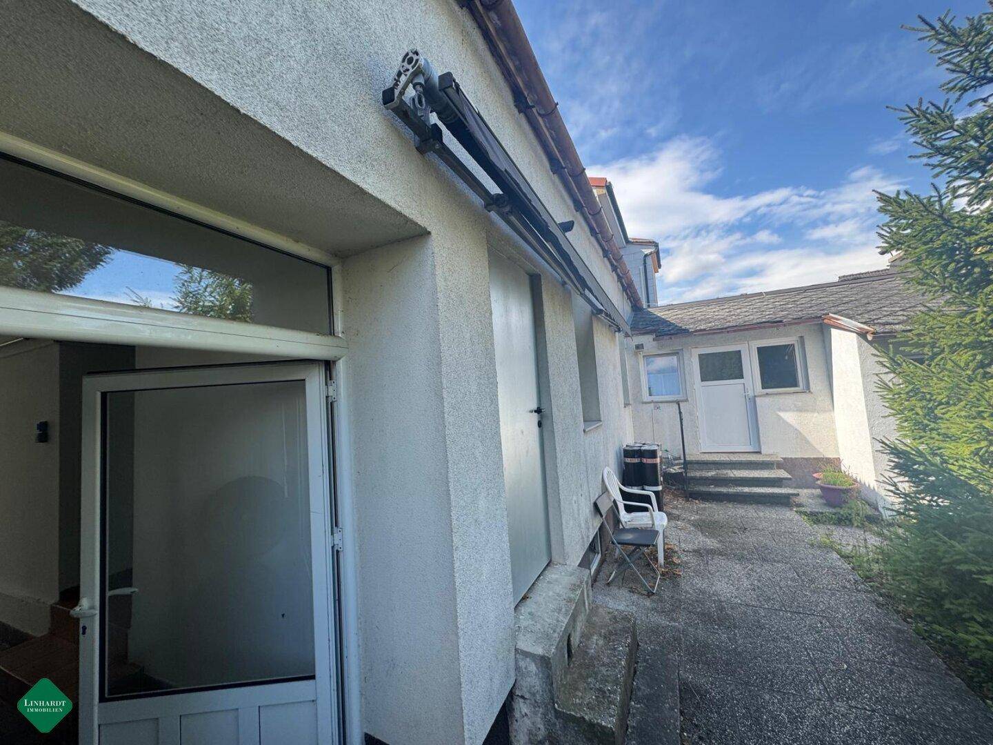 Seitenansicht des Hauses mit einem gepflasterten Weg und mehreren Türen, umgeben von Grün.