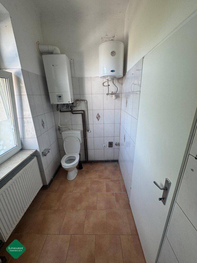 Kleines WC mit Fenster, Boiler und Gastherme, gefliest in Weiß und Braun.