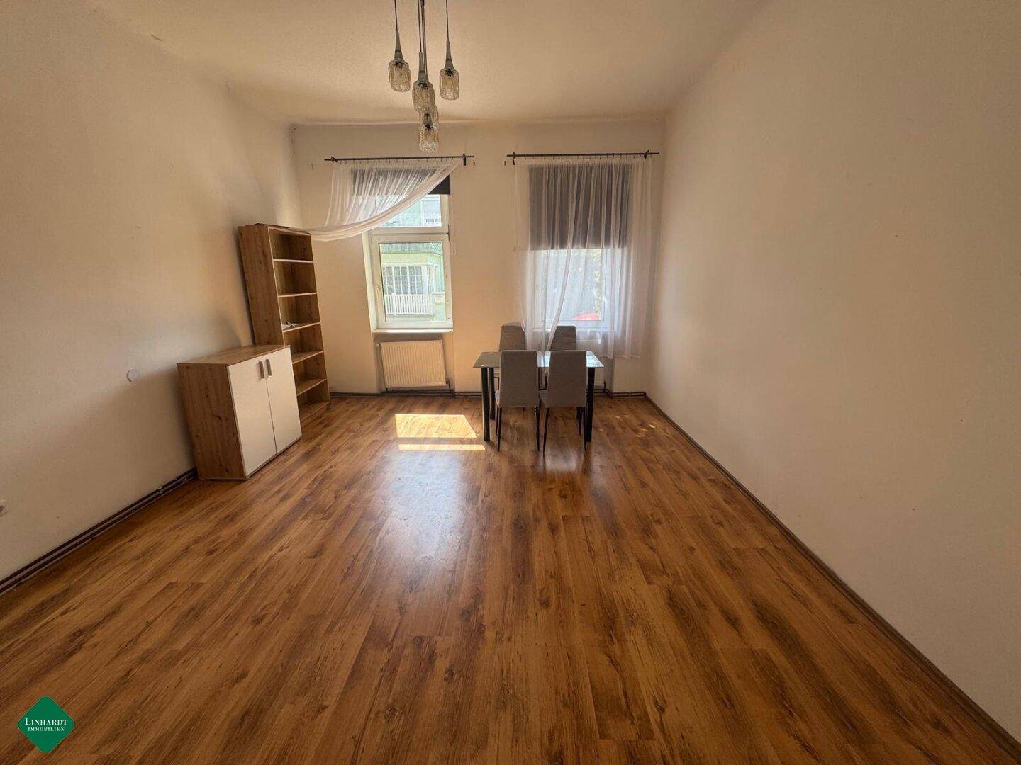 Geräumiges Wohnzimmer mit Laminatboden und einem kleinen Esstisch, hell und funktional.