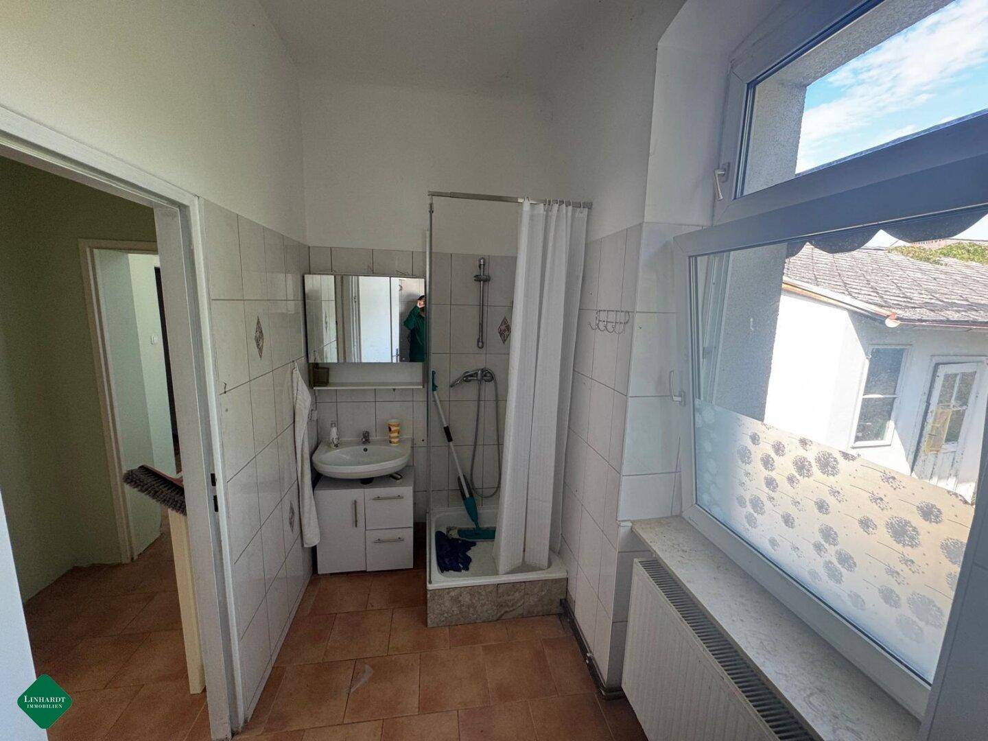 Badezimmer mit Dusche, Waschbecken und Fenster, gefliest in Weiß und Braun.