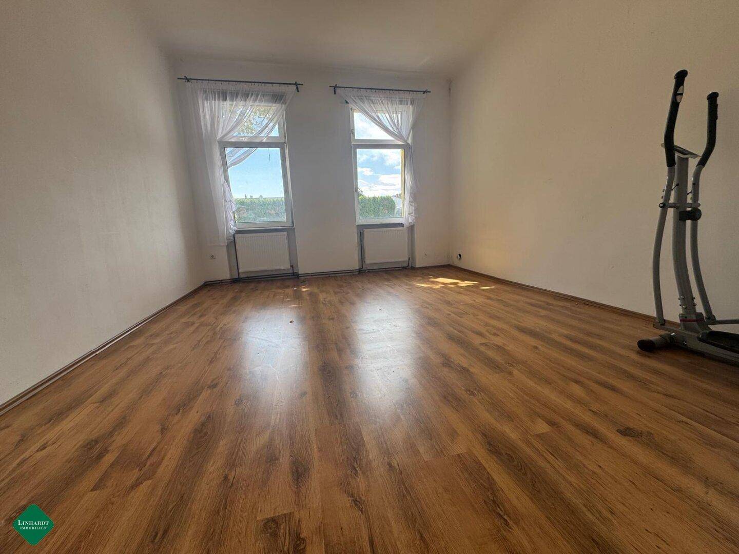 Helles Schlafzimmer mit Laminatboden und zwei Fenstern, ideal für Sportgeräte oder als Gästezimmer.
