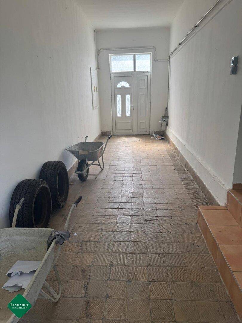 Langer Eingangsbereich mit gefliestem Boden und weißer Haustür, bietet Platz für Abstellmöglichkeiten.